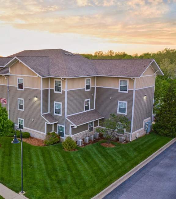 A large apartment complex with a grassy front yard and trees.