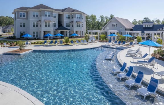 a swimming pool with chairs and umbrellas in front of an apartment building