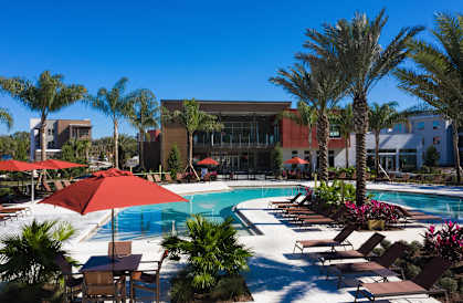 a swimming pool with umbrellas and palm trees in front of a building at Luxor Club, Jacksonville, FL