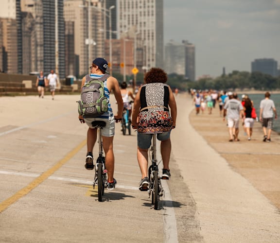 Two people riding bikes on a concrete path near a body of water.