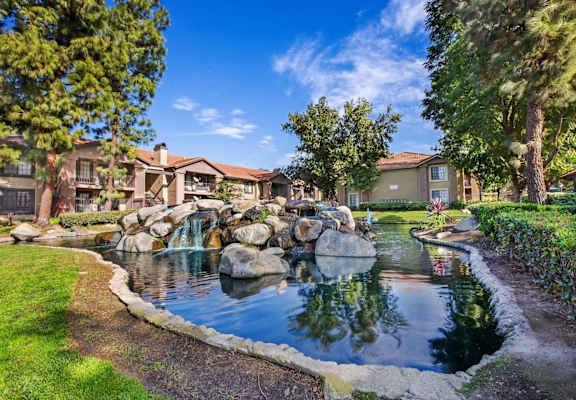 a fountain in the middle of pond surrounded  a grassy area with buildings in the background  at Citrine Hills, Ontario, CA, 91761