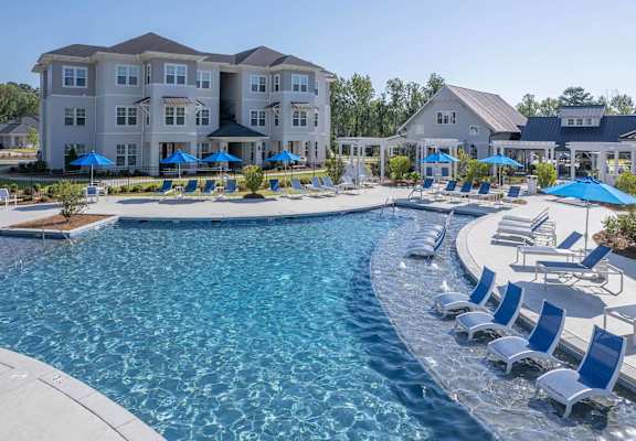 a swimming pool with chairs and umbrellas in front of an apartment building