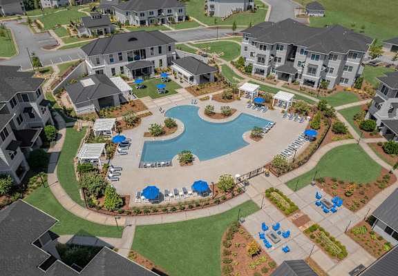 A large swimming pool surrounded by blue lounge chairs and umbrellas is the centerpiece of a resort-style community.