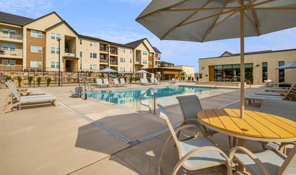 A sunny day at the poolside with chairs and an umbrella.