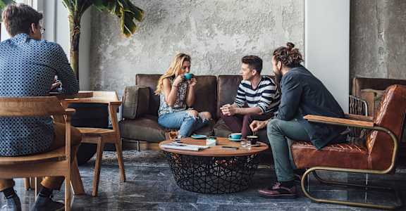 A group of people are sitting in a room with a large plant in the corner.