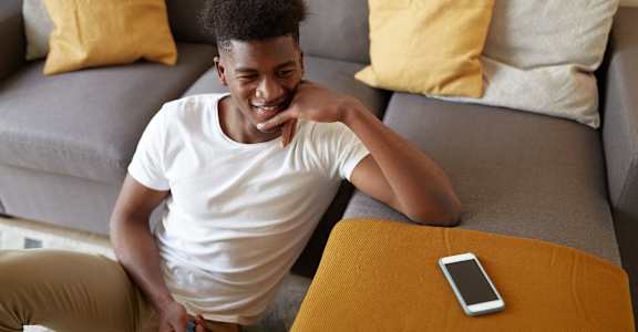 A man is sitting on a grey couch with a white t-shirt and khaki pants.