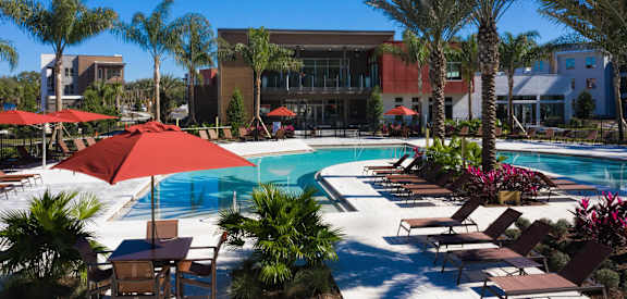 a swimming pool with umbrellas and palm trees in front of a building at Luxor Club, Jacksonville, FL