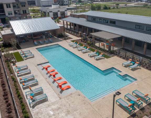 an aerial view of a swimming pool with chaise lounge chairs and a building in the background