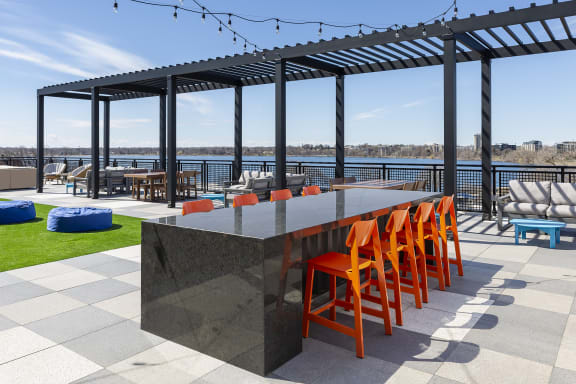 a dining table with orange chairs on a patio with a river in the background