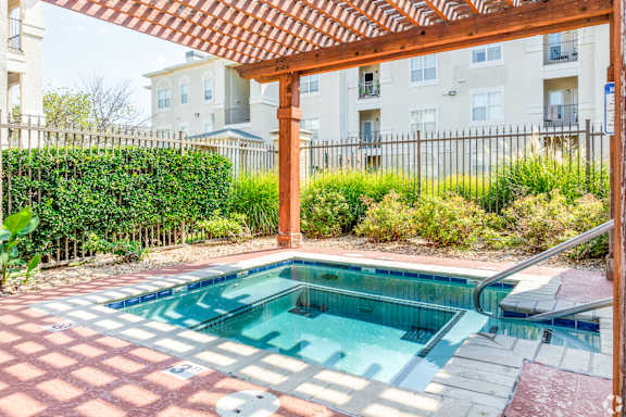 A small pool with a red tile border and a wooden pergola over it.