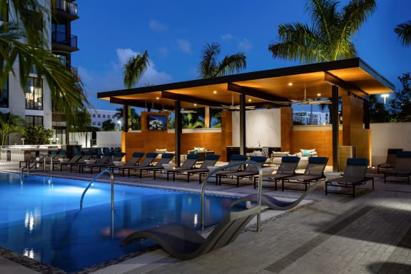 a swimming pool with chaise lounge chairs and a sunshade at night
