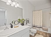 Thumbnail 3 of 8 - A bathroom with a white sink, toilet, and a mirror with lights above it.