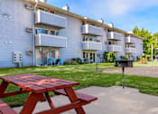 Thumbnail 7 of 8 - A red picnic table is in front of a white apartment building at Ironwood Apartments, Coeur d'Alene, Idaho