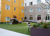 Thumbnail 13 of 16 - A large rock sits in a grassy area in front of a yellow building.