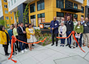 Thumbnail 14 of 16 - A group of people are gathered in front of a building for a ribbon cutting ceremony.