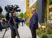 Thumbnail 15 of 16 - A man in a blue jacket is being interviewed by a camera crew.