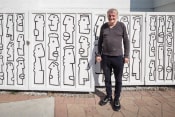 Thumbnail 1 of 9 - Artist that painted the building art is standing in front of a wall he painted