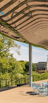 A park with a large shaded area and a person riding a bike.