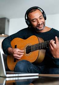 A man is playing guitar and using a laptop.