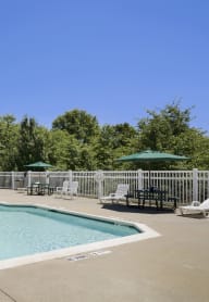 a pool with chairs and umbrellas and a fence around it at Boulder Pointe Apartments in Middletown, NY 10940