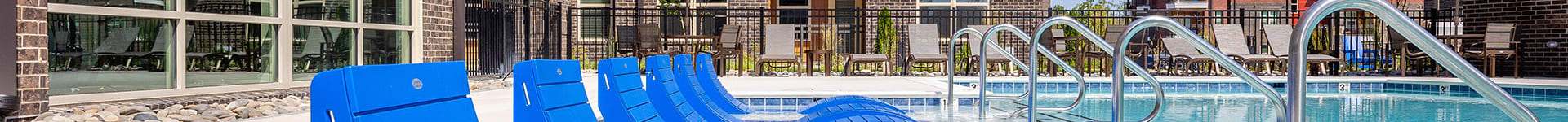 a pool with blue lounge chairs in front of an apartment building