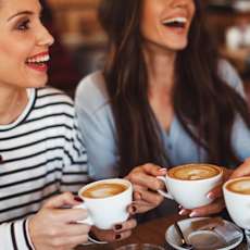 Three women are laughing and holding coffee cups.