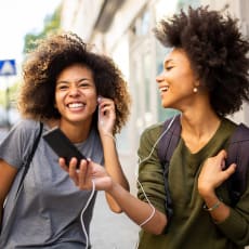 two women talking on the street while one is talking on a cell phone