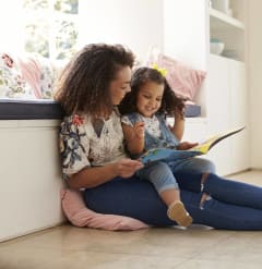 Mother Sitting on Floor with Daughter while Reading Book Together