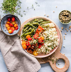 A bowl of couscous with vegetables and herbs on a table.