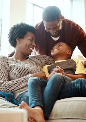 A family of three is sitting on a couch together.