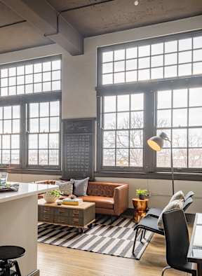 A modern kitchen with a bar stool and a table with a lamp.