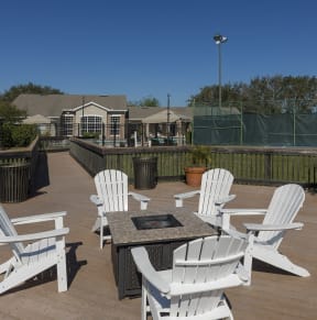 a patio with white chairs and a fire pit on a wooden deck