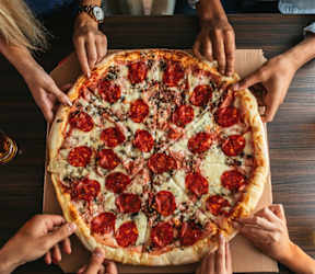 A large pepperoni pizza surrounded by people's hands.