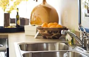 A kitchen sink with a bowl of oranges on the counter.