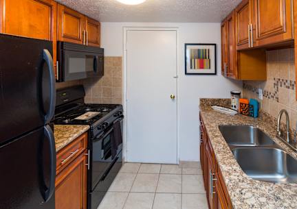 A kitchen with a black refrigerator, black microwave, black oven, and a white door.