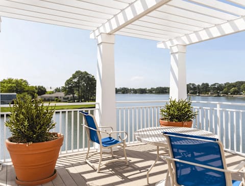 A white pergola with blue chairs and plants on a deck overlooking a body of water. at River House Apartments, Norfolk, VA