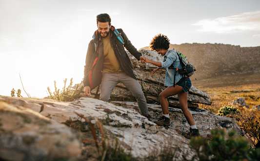 A man and a woman are hiking up a rocky hill.