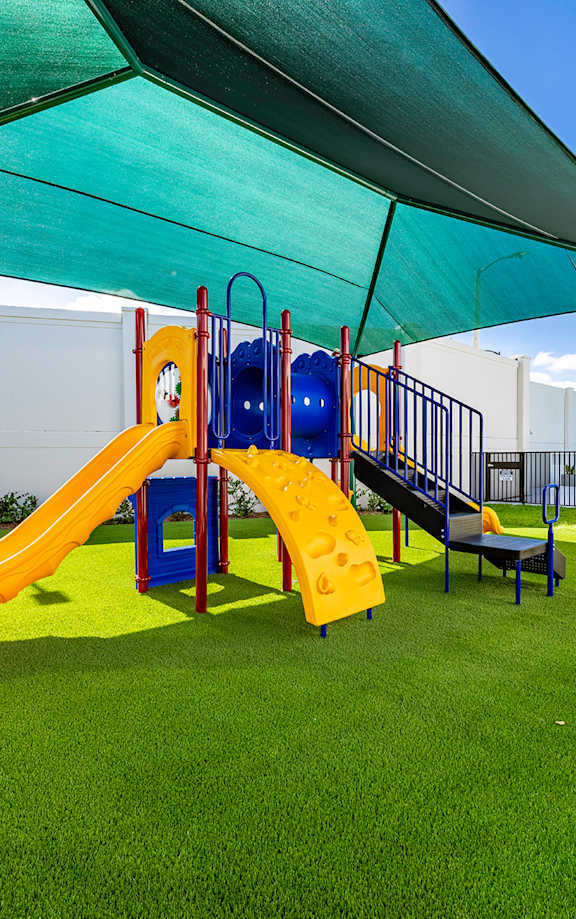 A playground with a yellow slide and a blue slide under a green canopy.