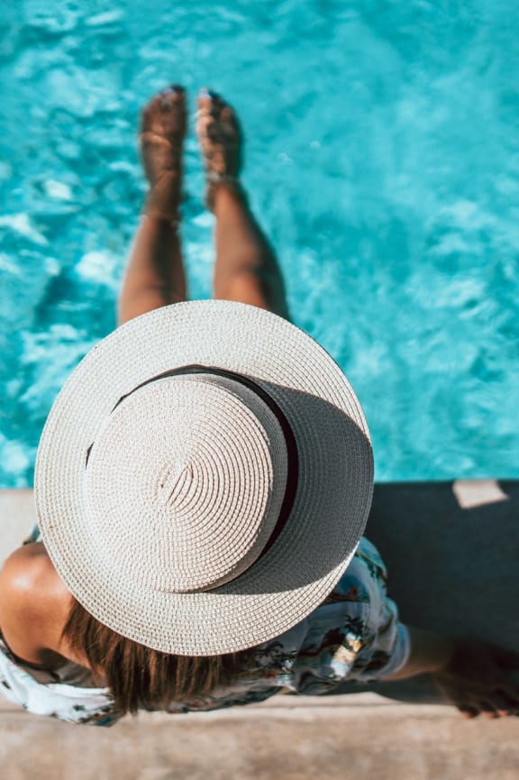 a woman laying on the side of a pool with her hat