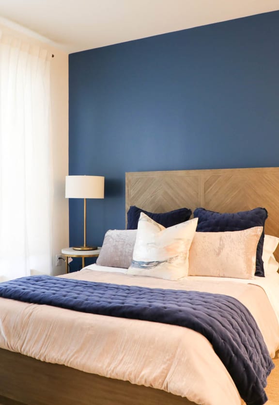 a bedroom with a blue accent wall and a bed with a wooden headboard at The Met at Metro Centre Apartments, Owings Mills