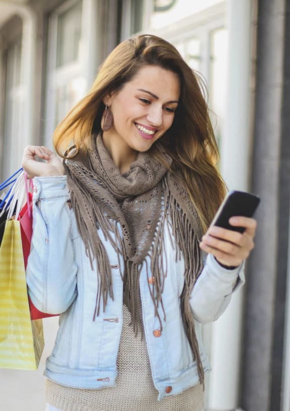 a woman looking at her cell phone while holding shopping bags