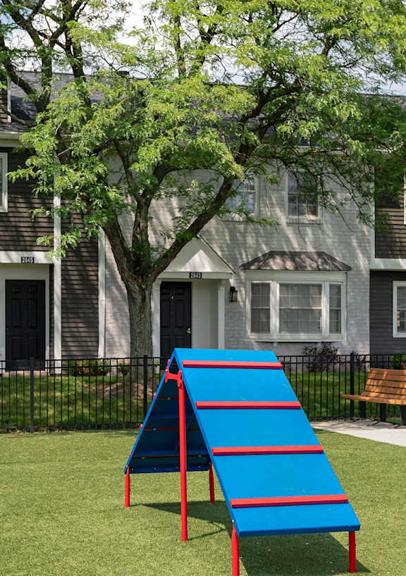 A playground with a blue slide in front of a grey building.