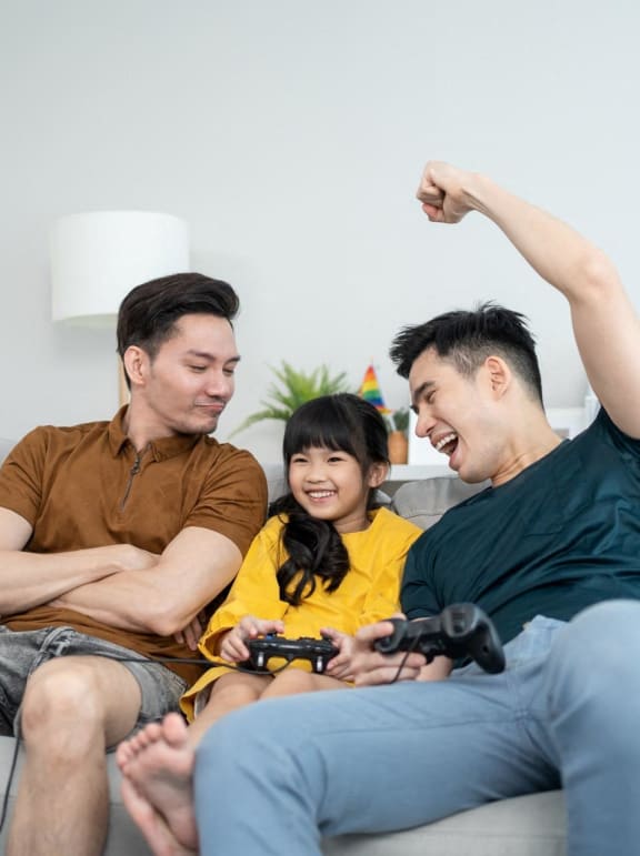 Fathers Sitting on Sofa with Daughter Playing Video Games