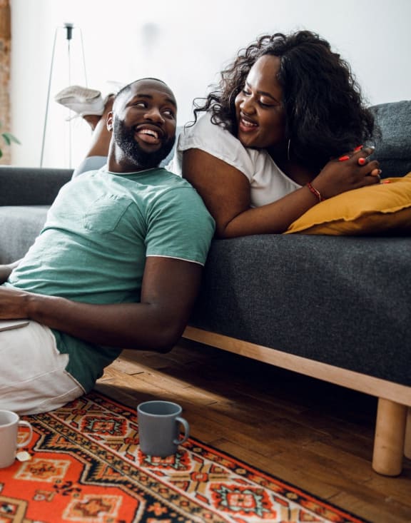 Woman Laying on Sofa Smiling at Boyfriend Sitting on Floor with Laptop at Koi Apartments, Seattle, Washington