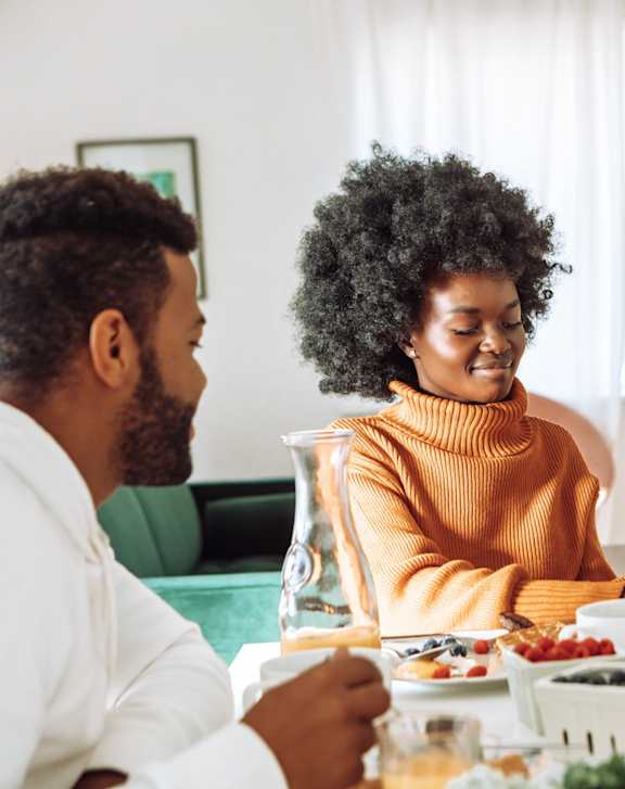 a family sitting at a table eating breakfast and looking at a laptop