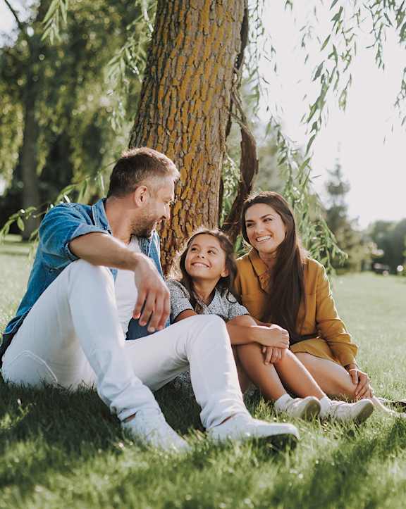 Three people sitting on grass under a tree.