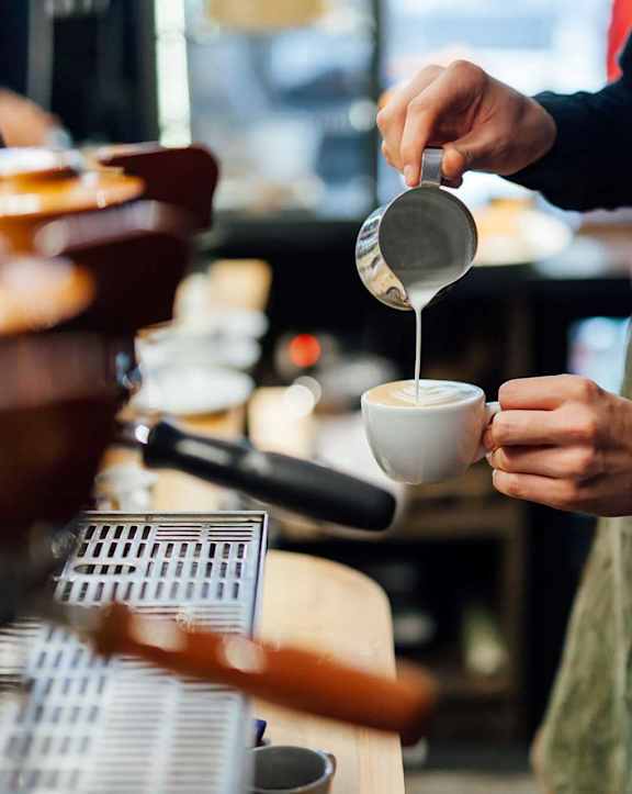 A person in an apron is pouring a liquid from a container into a cup.