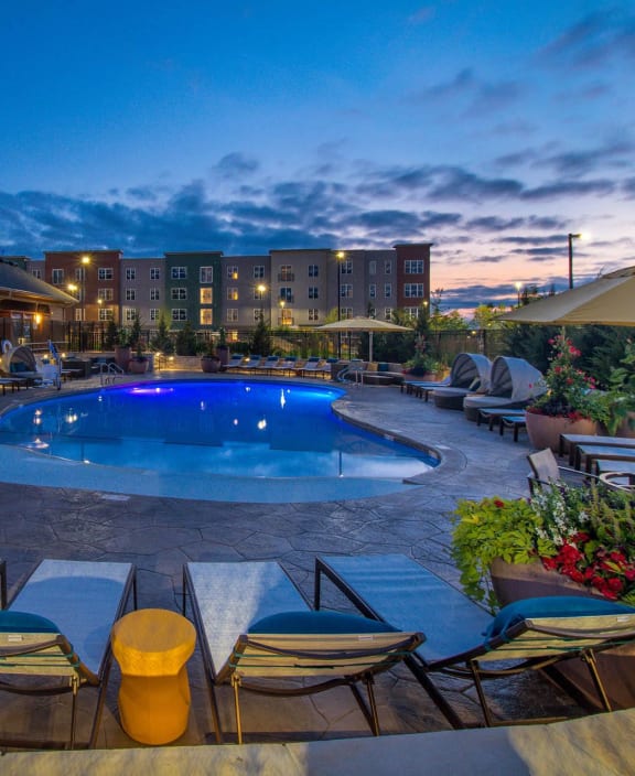 a swimming pool at night with chairs and umbrellas