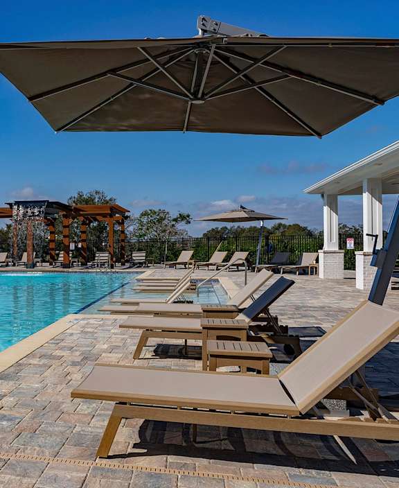 A pool with sun loungers and a building in the background at The Waverly at Winter Haven Apartments, Winter Haven, 33884