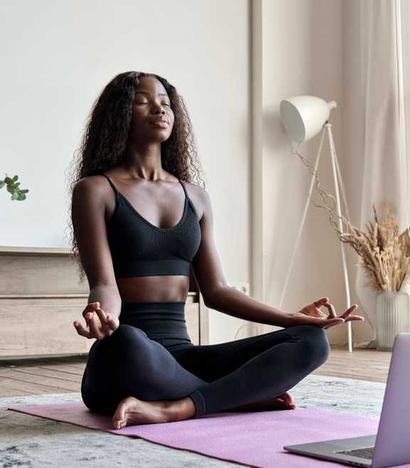 Woman Practicing Yoga while Sitting in Front of Laptop in Living Room